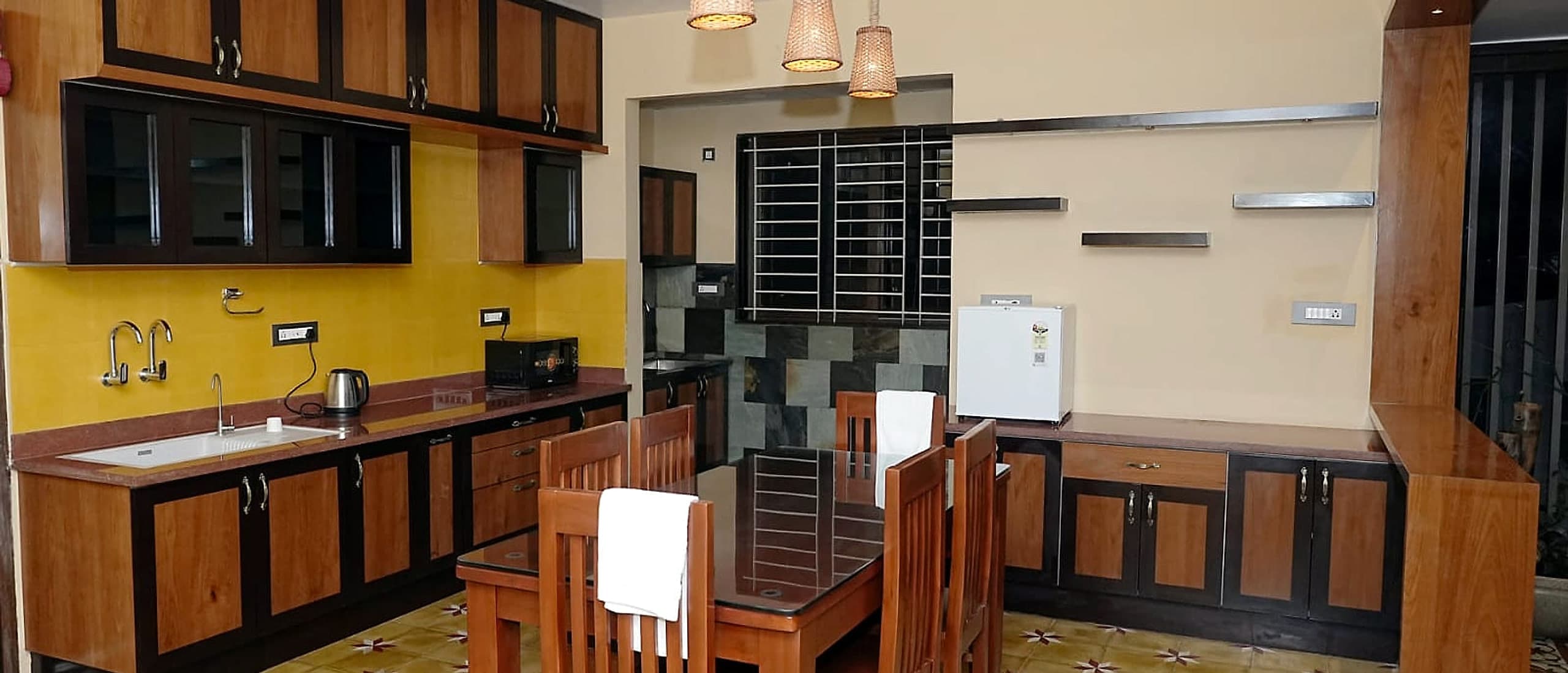 A kitchen and dining table under woven pendant shades, on a floor of patterned tiles.